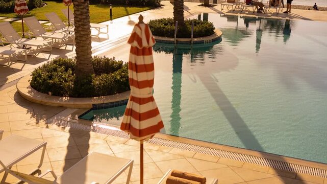Panning showing red-white umbrella staying closed on resort deck, two people in swimwear strolling