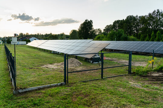Dabrowa Gornicza, Poland - 23 August 2026: View of a solar farm with rows of photovoltaic panels installed on a grassy field, enclosed by a metal fence under a soft evening sky.