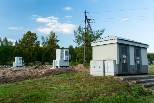 Dabrowa Gornicza, Poland - 23 August 2026: View of electrical substation equipment and a utility building set in a grassy field with trees and power lines under a blue sky.