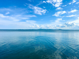 Fototapeta premium Calm water reflects blue sky with clouds over a distant landscape in the early afternoon