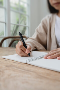 Close-up of a hand writing in a spiral notebook on a wooden desk. Ideal for planning, journaling, productivity and business concepts.
