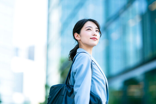 オフィス街で前向きに空を見上げる若い日本人女性、通勤やキャリアを表現した爽やかなビジネスポートレート