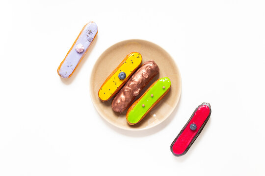 Colorful gourmet eclairs with glazed topping on plate - modern pastry flat lay in soft natural light, top view dessert concept