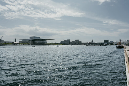 Copenhagen, Denmark - 23 August 2026: View of the Copenhagen Opera House across the harbor with modern architecture and boats on the water under a cloudy sky.