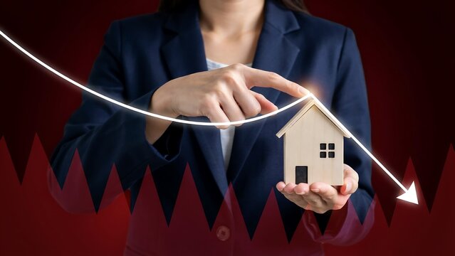 Professional holding miniature house model with downward trending arrow graphic representing real estate market decline