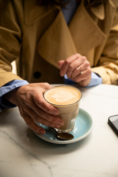 Close-up of a woman's hand holding a cappuccino cup on the terrace of a caf&eacute;