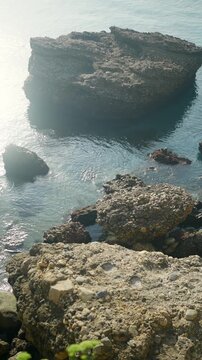 Rocky coast of Nerja with calm turquoise water and sun flare on a summer day in Andalusia, Spain