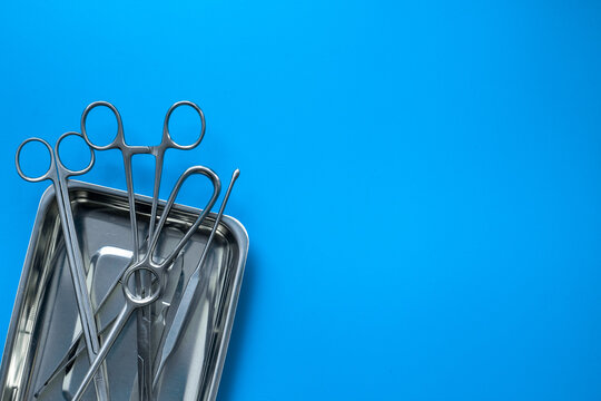 Sterile surgical instruments and tools - scalpels, scissors and others - in a stainless tray on blue background, top view