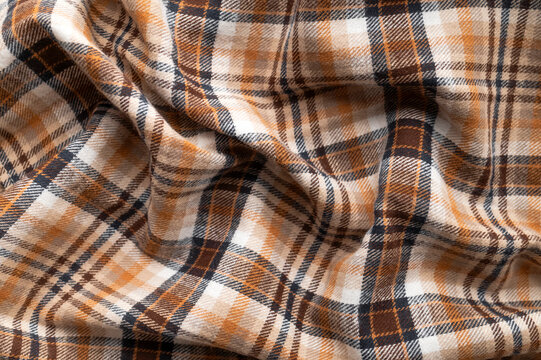 Plaid cotton shirt fabric appears in closeup with warm brown checks, soft folds and woven textile texture, supporting flannel styling, garment material, sewing education and fashion retail imagery.
