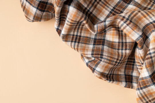 Plaid fabric in cozy autumn shades of brown, orange, beige with soft folds on beige background top view with space for text. Concept of natural cotton flannel fabric for sewing shirt, textile branding