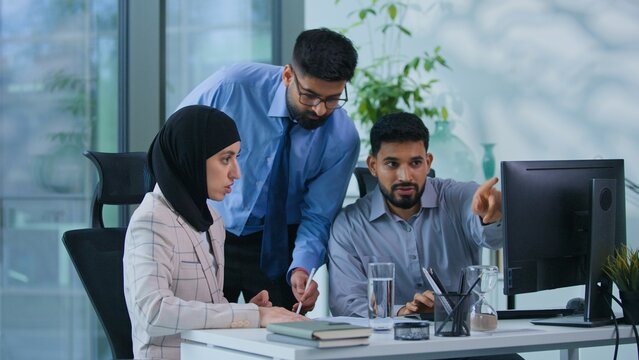 Arabian business team three Muslim professionals talking argue with papers and computer in office. Indian boss angry irritated talk writing notes argue with businesswoman in hijab businessmen quarrel
