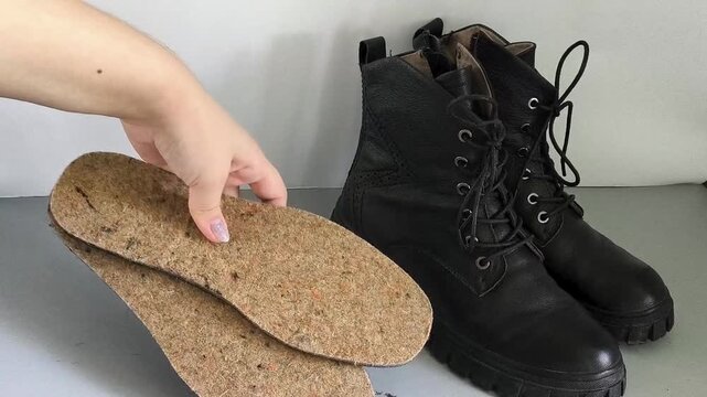 The woman places warm felt shoe insoles next to her boots, preparing footwear for autumn and winter, providing warmth and protection from the cold weather.