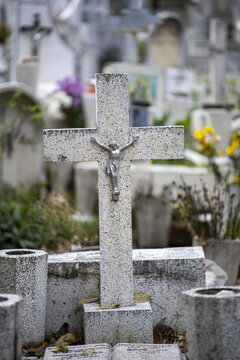 Patzcuaro, Michoacan, Mexico - 27 October 2021: View of a stone cross with a metal crucifix in a cemetery decorated for Dia de los Muertos, featuring weathered grave markers and scattered flowers.