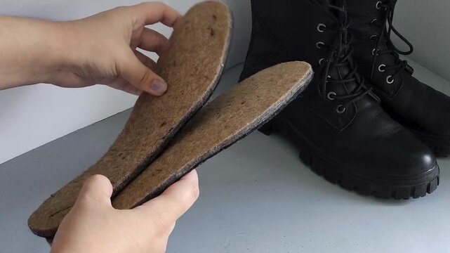 Close up of felt thermal insoles in a woman's hands with boots in the background, warm footwear, winter shoe insulation and protection from cold weather.