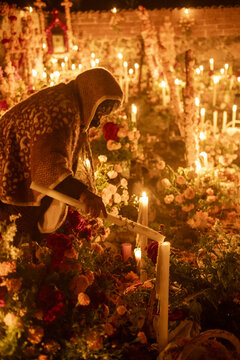 Patzcuaro, Mexico - 01 November 2023: View of an elderly woman lighting candles on a grave decorated with marigolds during the Day of the Dead celebration at Lake Patzcuaro.