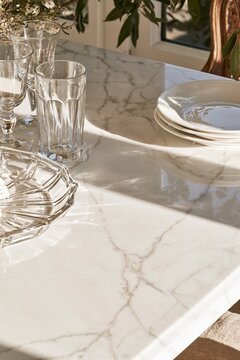 Closeup of white marble table surface with soft grey veining, crystal glassware, and plates in a Parisian dining room setting