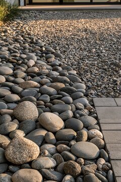 Closeup of smooth river stones and gravel forming a decorative border along a modern driveway, illuminated by warm evening light