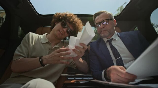 Young adult Caucasian man and middle aged businessman reviewing contract in car, young man crumpling and throwing paper. Video suitable for corporate conflict and contract rejection themes