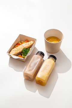 Healthy meal prep ration with grilled salmon fillet vegetables pumpkin puree soup and two smoothies on white background