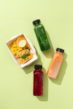 Diet lunch box with rice cutlets sauce and three colorful detox smoothie bottles on pastel green background