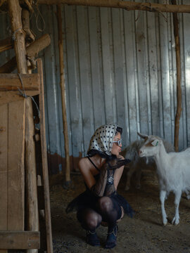 Asian woman crouching blowing kiss white goat inside barn