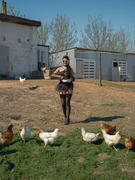 Asian woman walking and feeding chickens from bowl on farm yard