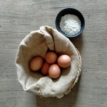 saquito con 5 huevos marrones y cuenco negro con harina  pegado al lado del saco