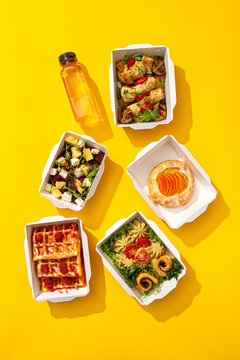 Daily healthy food delivery ration with waffles meat salad pastry and juice in containers on yellow background