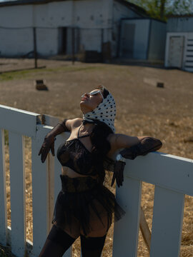 Asian woman leaning white farm fence looking up sunny day