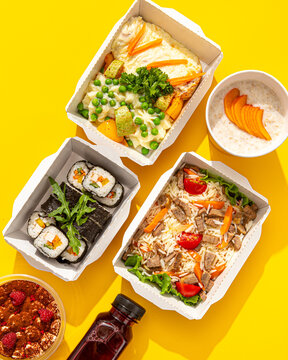 Assorted daily healthy meal ration with sushi rice dessert and beverage in takeaway boxes on yellow surface
