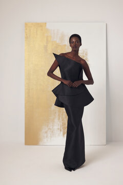 Black fashion model wearing asymmetrical one-shoulder structured black satin top and skirt