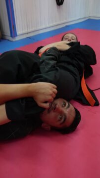 Young woman practicing hapkido ground fighting with a male partner. She performs a submission grappling technique on the tatami mat in a dojo