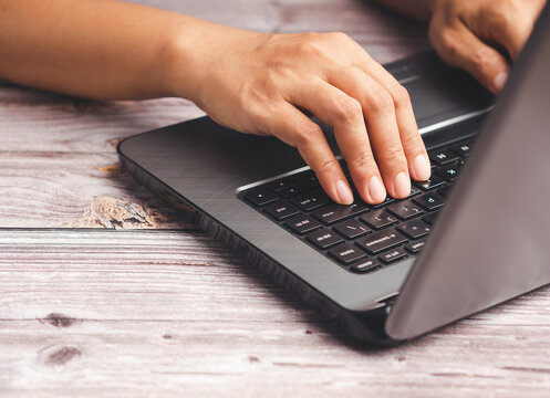 Hand Typing on Laptop Keyboard at Wooden Table