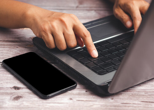 Hand Typing on Laptop Keyboard Beside Smartphone
