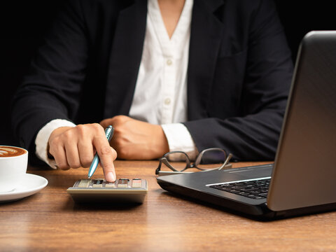 Person Using Calculator Beside Laptop at Wooden Desk