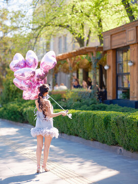 Asian woman back view holding purple heart balloons on street