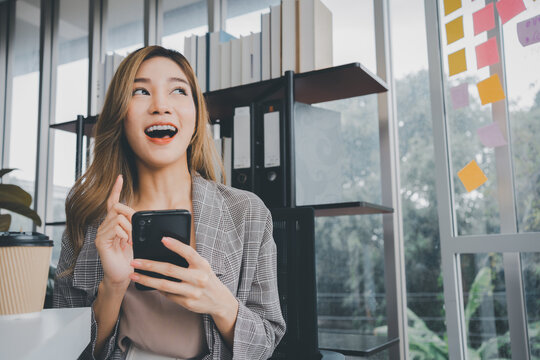 A young entrepreneur reacts with excitement while reading good news on her smartphone in a modern office. The expressive portrait represents startup success, business growth, and digital achievement