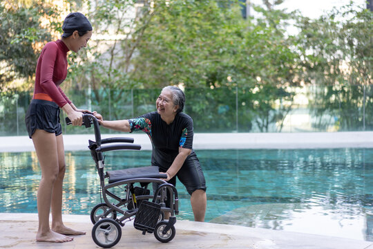 A caregiver assists a senior woman with a wheelchair after an aquatic therapy session beside an outdoor swimming pool. The scene represents accessibility, rehabilitation, and inclusive healthcare