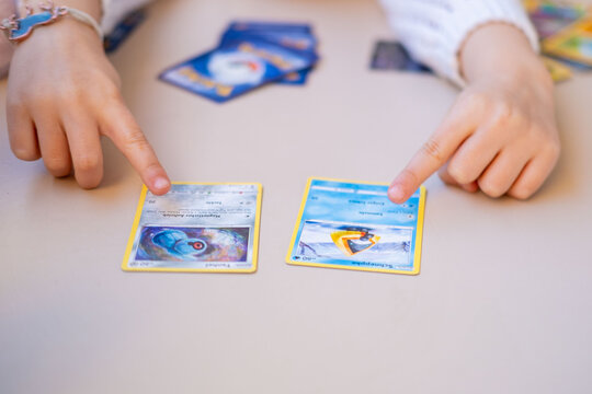 Young enthusiast Child holding Pokemon card, Collecting trading cards with Pokeball logo on white table, close up hands playing, sorting trading card game, Battle with friends, childhood Fan Culture