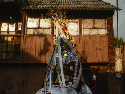 Angahuan, Michoacan, Mexico - 24 July 2026: View of a performer in a traditional Moros y Cristianos dance costume with an elaborate, colorful headdress standing before a rustic wooden building.