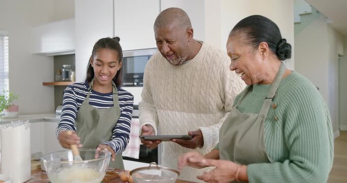 African American family baking at kitchen island, teen girl stirring bowl following tablet recipe