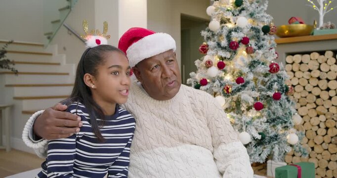 Senior African American grandpa pointing to Christmas tree while granddaughter talking and looking