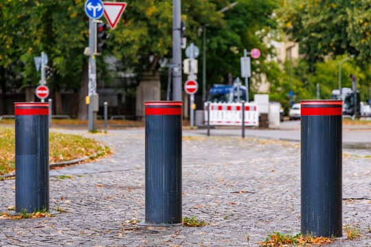 Three black retractable bollards with red reflective stripes on cobblestone street, urban security and traffic control concept