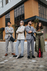 Fototapeta premium A confident business team of four young professionals stands with arms crossed outside a modern office building.