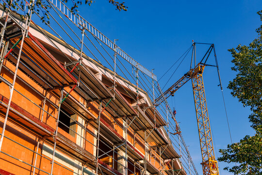 Residential building under construction with metal scaffolding and yellow tower crane against clear blue sky, real estate development concept