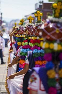 Uruapan, Mexico - 31 March 2024: View of Aguadoras carrying traditional water vessels adorned with colorful flowers during a cultural procession in Uruapan.