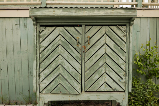 Exterior view of a green colored wooden garbage bin that has a herringbone design decorating the doors.