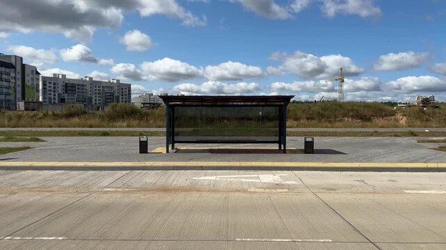 Empty modern bus stop shelter with glass panels in new development area with apartment buildings and construction crane. urban transport, public infrastructure, development