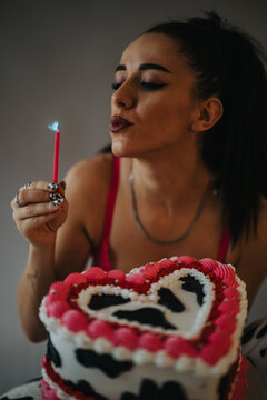 Young woman blows out a candle on a heart-shaped birthday cake. She leans forward to extinguish the flame during a small celebration.