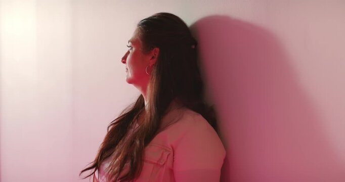 Mature African American woman leaning in studio in light jacket, hoops, pink light making shadow